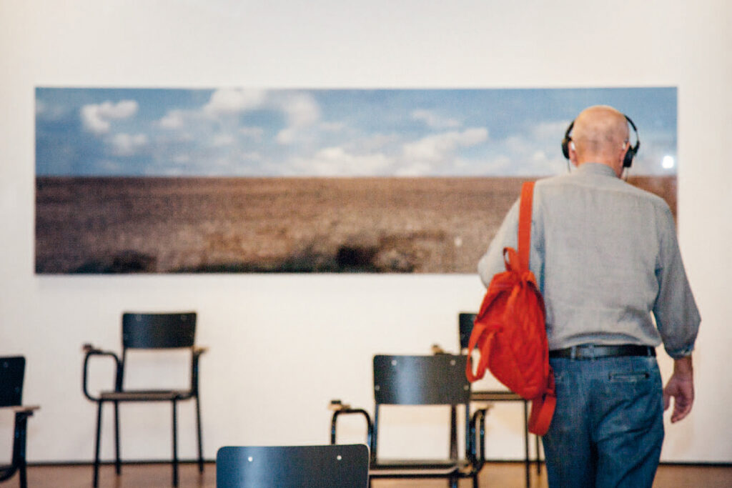 Besucher mit Kopfhörer in der Klanginstallation 2014 Horchposten/Postes d’écoute 1914 vor einem Landschaftsbild.